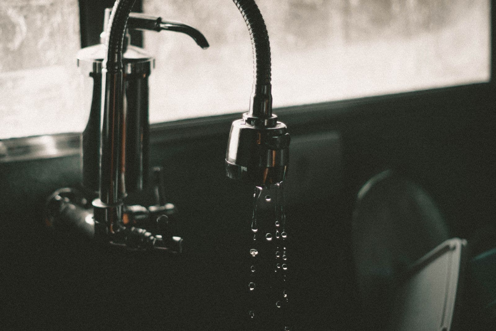A black kitchen tap with water running from the spout. Illustration of a small leak.